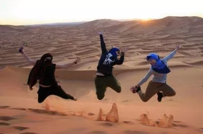 Three travellers jumping on a dune at sunset in the Sahara, Morocco