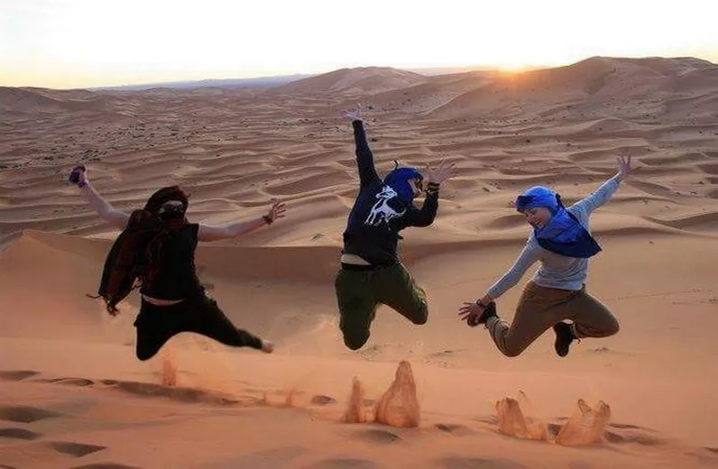Three travellers jumping on a dune at sunset in the Sahara, Morocco