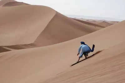 Sandboarding down a steep dune face at Erg Chigaga, Morocco