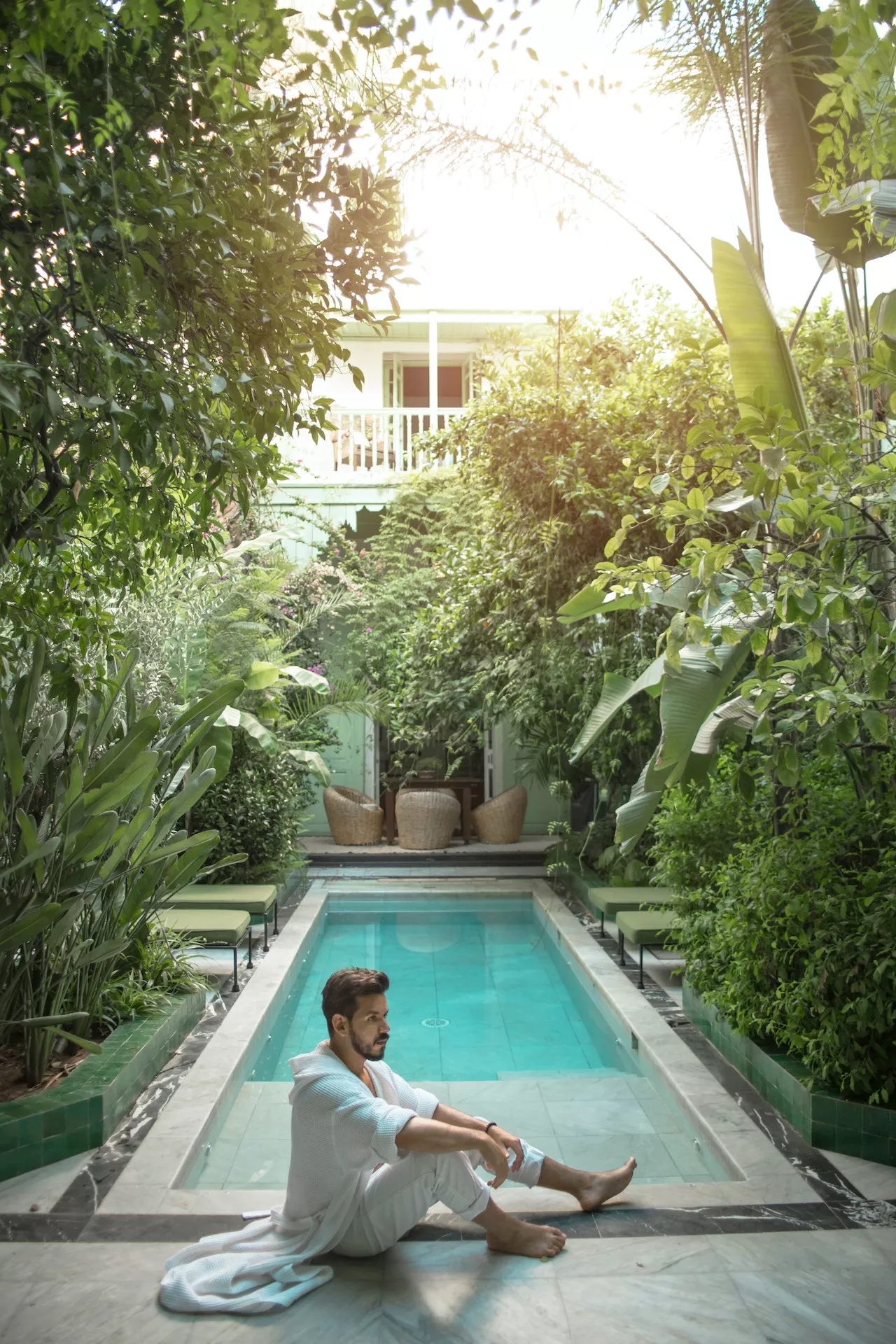 Traveller sitting beside a riad courtyard pool among plants, Marrakech