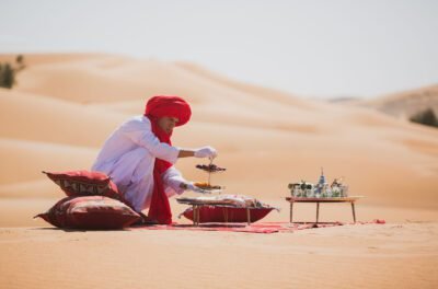 Guide in a red turban serving tea on rugs on the dunes, Morocco