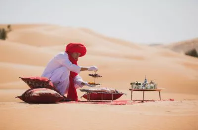 Guide in a red turban serving tea on rugs on the dunes, Morocco