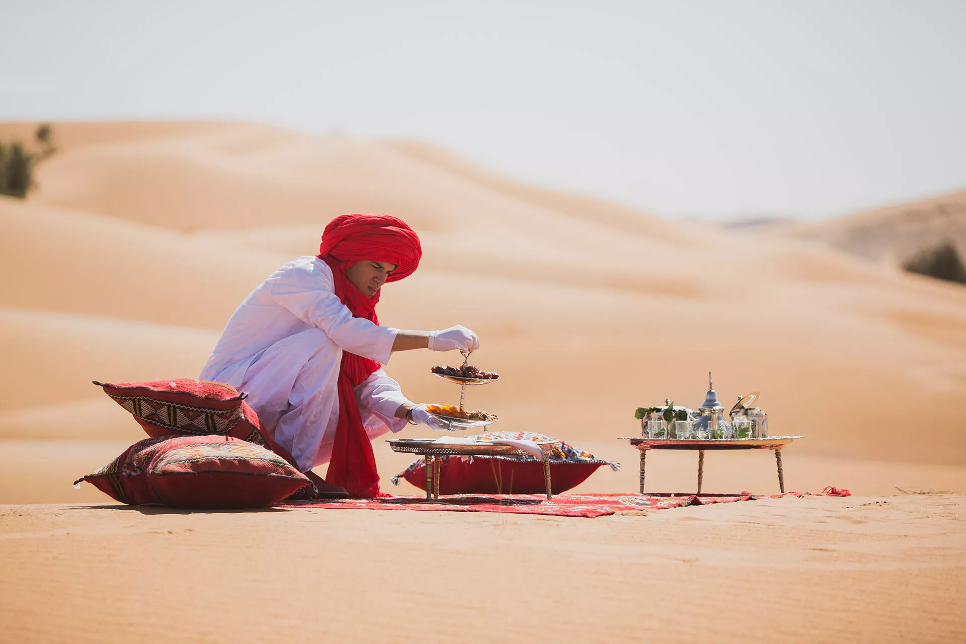Guide in a red turban serving tea on rugs on the dunes, Morocco