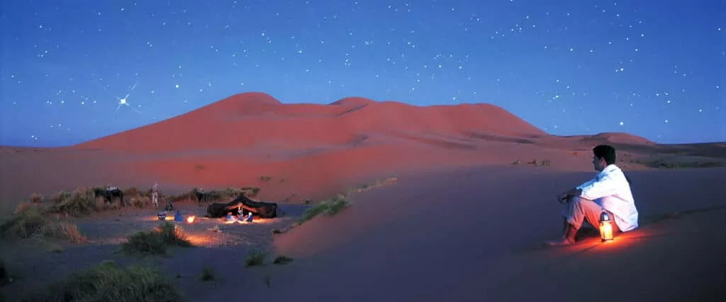 Traveller sitting by a lantern at a desert camp under a starry sky, Morocco