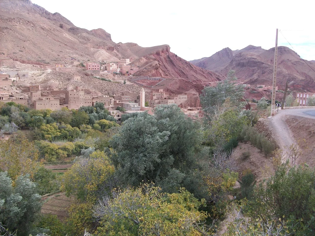 Snow-capped peaks of the High Atlas Mountains rise above a green valley in Morocco.