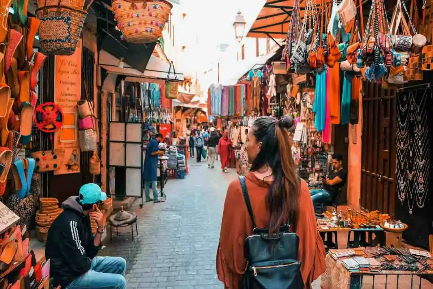 Traveller walking through a colourful souk in the Fez medina, past leather bags, slippers and lanterns, Morocco
