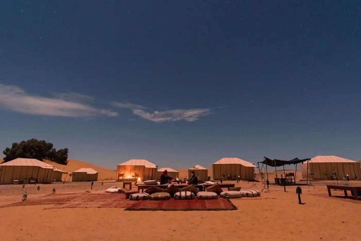 Couple dining by lantern light at a private Sahara desert camp under a starry night sky, Morocco