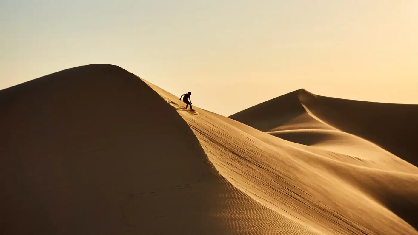 Silhouette of a traveler sandboarding down a dune at sunset in the Moroccan desert